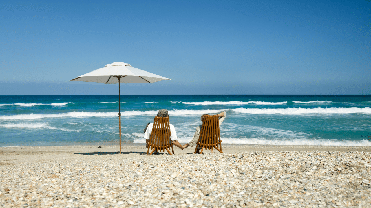 Two people sitting in chairs on the beach next to a white umbrella.