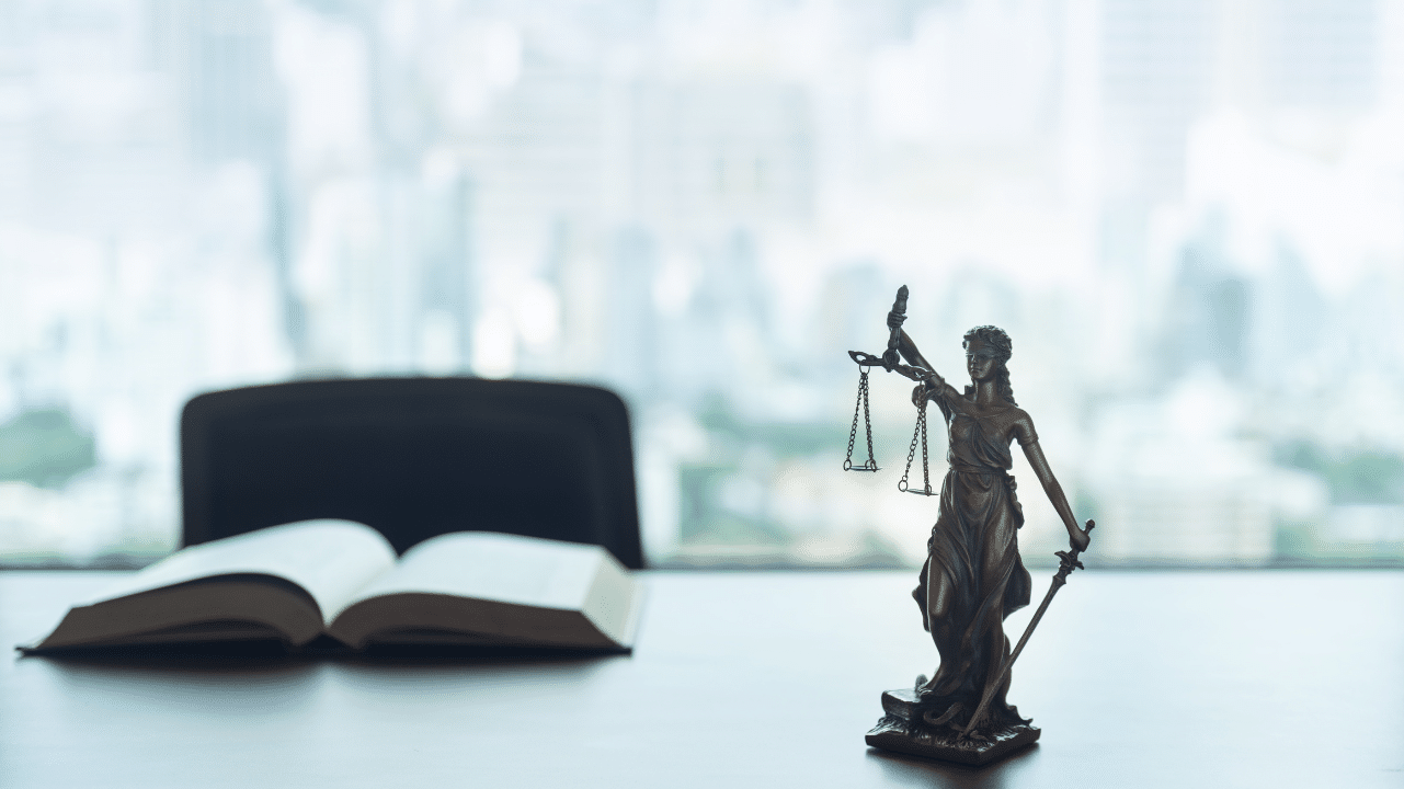 Statue of justice and law books on desk in lawyer office with blurred city view in background.